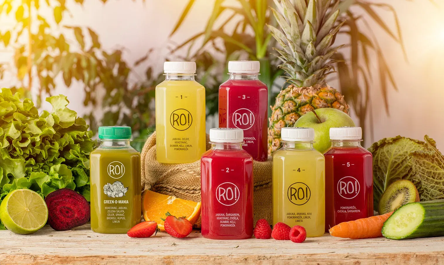Five colorful RO! cold-pressed juices arranged with fresh fruit and vegetables